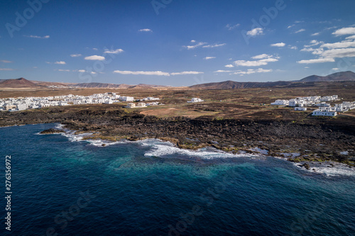 Drone view of a spanish island, volcano beach, blue sky, clouds , white houses on the coast, pastel tons, Lanzarote. 