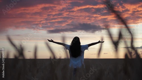 Woman with long hair standing in a wheat field at sunset spreading her arms to the side enjoying the beauty