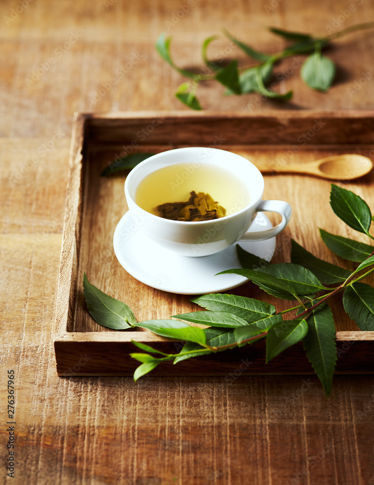 A cup of green tea on wooden tray with green leaves. Healthy lifestyle. Copy space A cup of green tea on wooden tray with green leaves. Healthy lifestyle. Copy space