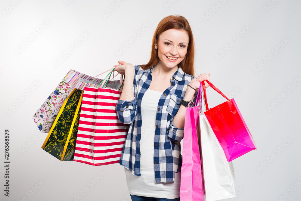 Young attractive smiling woman with many colored shopping bags on gray. Woman making shopping