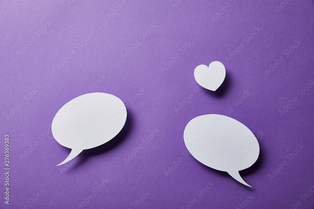 white speech bubbles and small paper heart on purple surface white speech bubbles and small paper heart on purple surface