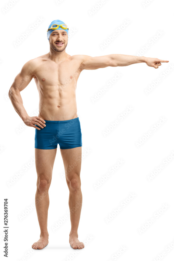 Young man in swimming shorts, googles and a cap pointing to the side Young man in swimming shorts, googles and a cap pointing to the side
