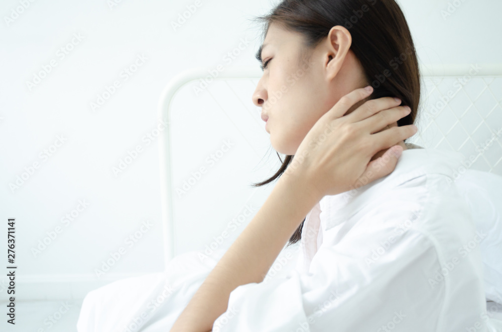 Asian women wear white pajamas in the bedroom. She has pain in the neck area. Asian women wear white pajamas in the bedroom. She has pain in the neck area.