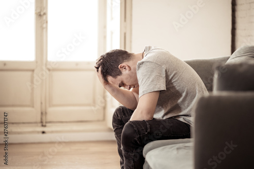 Young man suffering from depression lying on sofa alone at home feeling frustrated and hopeless