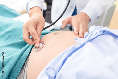 Doctor using hands and stethoscope listening to patient  pregnant tummy for health check up.