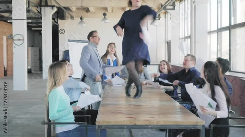 Female team leader starts dancing on the table. Colleagues dance with her. Employees celebrate success. Corporate party business team