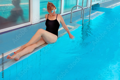 amazing stylish beautiful fit blonde woman in black swimming suit and sun glasses by the edge in the swimming pool. Summer. Vacation, recreation, wellness and sport concept. © k8most