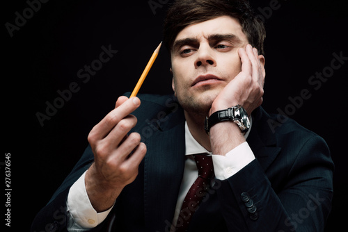 thoughtful businessman looking at pencil in hand isolated on black photo