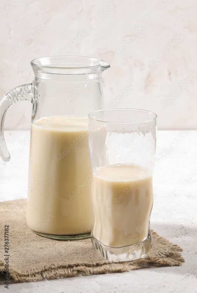 Close-up decanter and glass of oat milk on burlup napkin on white background. Close-up decanter and glass of oat milk on burlup napkin on white background.