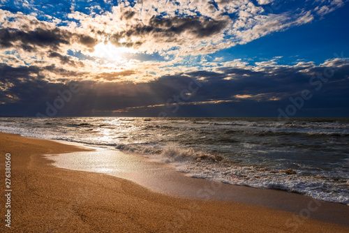 A beach with golden sand, small waves and a beautiful dramatic sky