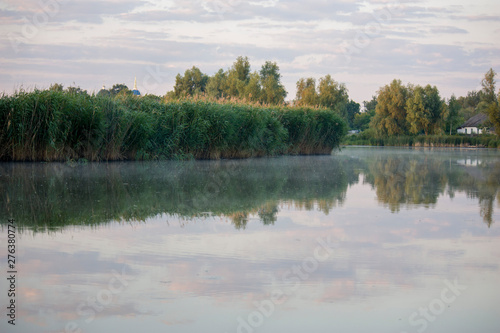Part of the lake with water and dry reeds and grass near the shore. Early in the morning with fog on the water. Natural Wild Background