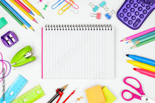 Blank, lined, coil notebook with school supplies frame against a white background. Back to school concept. Copy space.