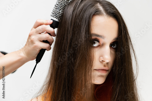 Photo portrait of the work of the master hairdresser makes a fashionable hairstyle with a hair dryer and a hairbrush in the studio on a white background. The brunette model has colored hair.