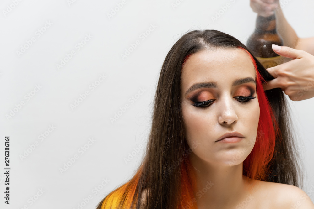 Fototapeta premium Photo portrait of the work of the master hairdresser makes a fashionable hairstyle with a hair dryer and a hairbrush in the studio on a white background. The brunette model has colored hair.