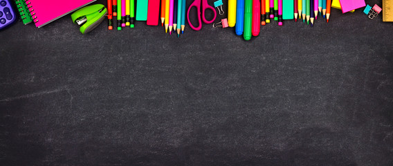 School supplies top border banner. Top view on a chalkboard background with copy space. Back to school concept.
