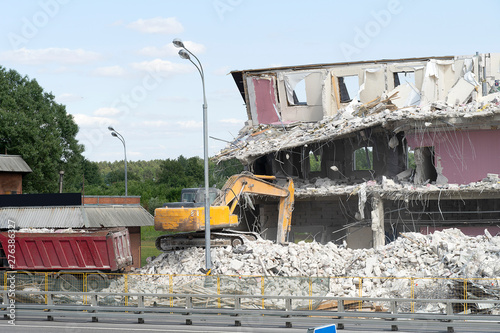 Yellow excavator picks up construction waste for loading onto a truck. Technique destroyed the building, is reinforcement, concrete and stones. Destroyed house, concrete, fittings.