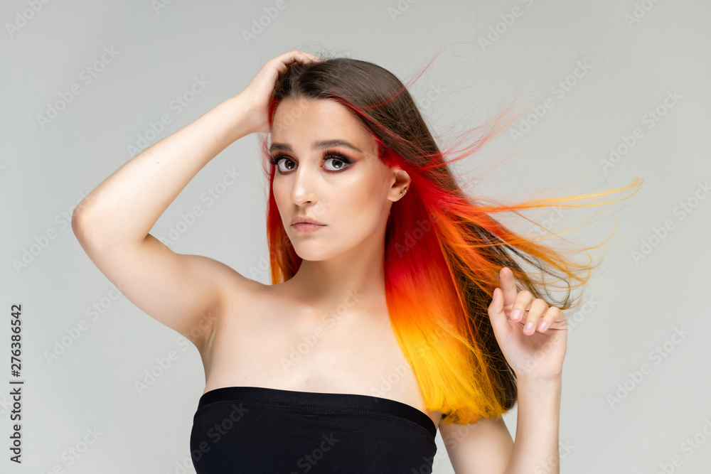 A close-up portrait photo of a fashionable hairstyle red-yellow in studio on a white background. The pretty brunette model with beautiful make-up has beautiful flowing colorful hair. A close-up portrait photo of a fashionable hairstyle red-yellow in studio on a white background. The pretty brunette model with beautiful make-up has beautiful flowing colorful hair.