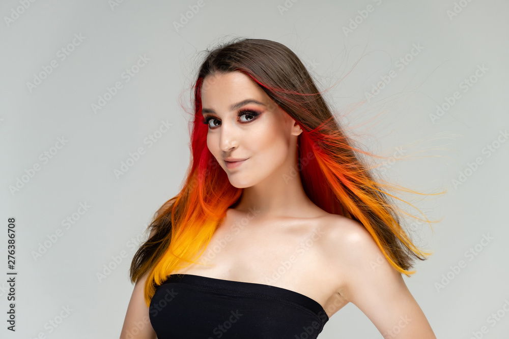 A close-up portrait photo of a fashionable hairstyle red-yellow in studio on a white background. The pretty brunette model with beautiful make-up has beautiful flowing colorful hair.