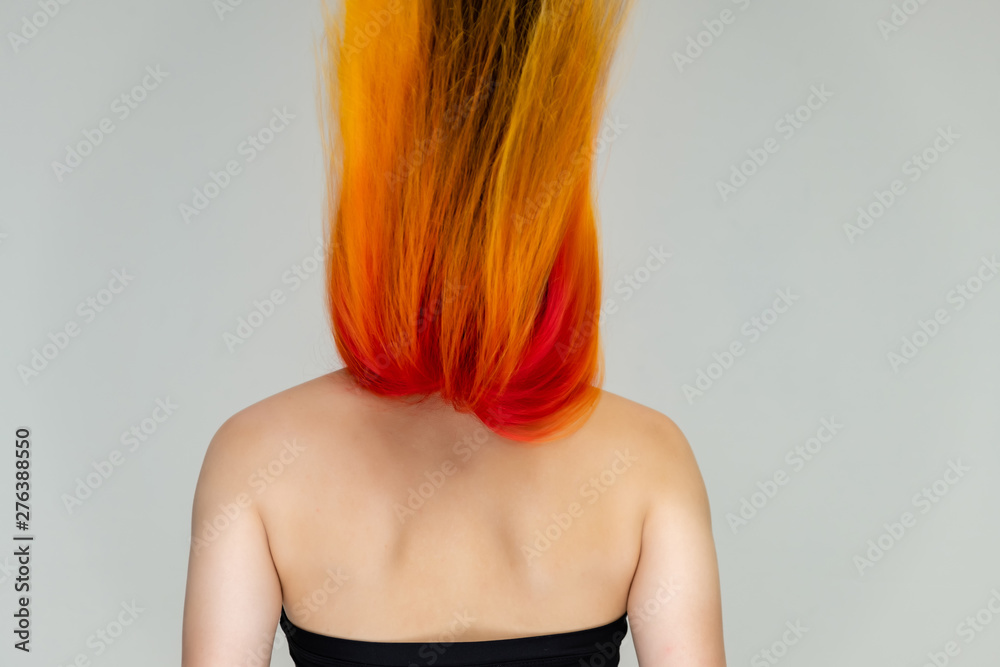 Obraz premium A close-up portrait photo of a fashionable hairstyle red-yellow in studio on a white background. The pretty brunette model with beautiful make-up has beautiful flowing colorful hair.