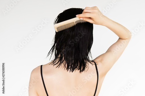 young brunette woman combing wet hair with wooden comb, hair care concept
