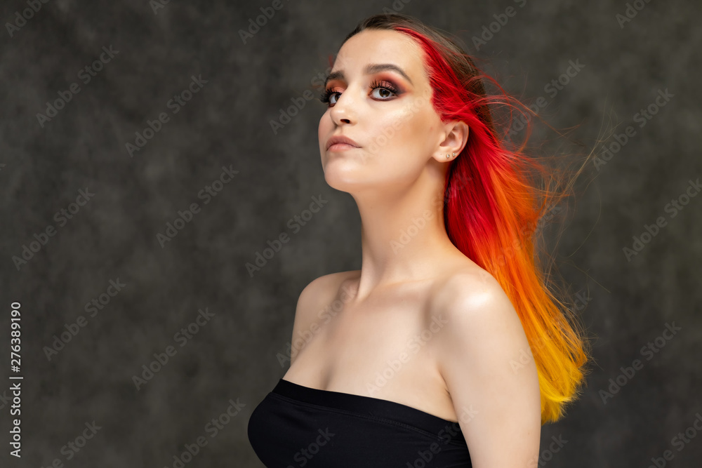 A close-up portrait photo of a fashionable hairstyle red-yellow in studio on a gray background. The pretty brunette model with beautiful make-up has beautiful flowing colorful hair.