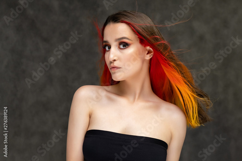 A close-up portrait photo of a fashionable hairstyle red-yellow in studio on a gray background. The pretty brunette model with beautiful make-up has beautiful flowing colorful hair.