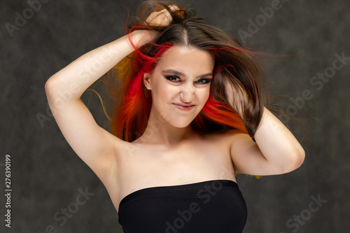 A close-up portrait photo of a fashionable hairstyle red-yellow in studio on a gray background. The pretty brunette model with beautiful make-up has beautiful flowing colorful hair. © Вячеслав Чичаев