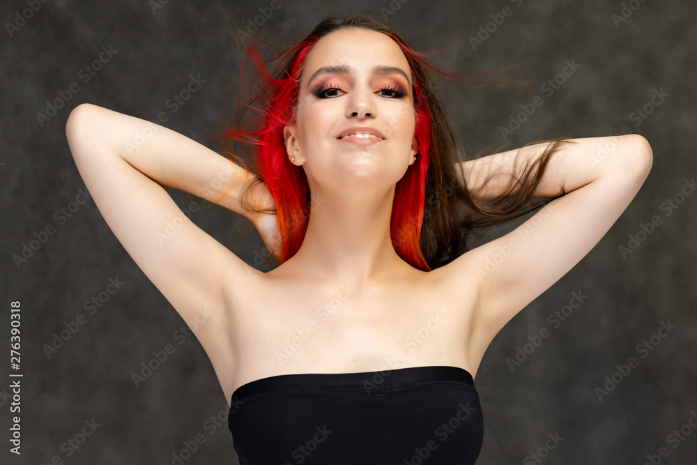 A close-up portrait photo of a fashionable hairstyle red-yellow in studio on a gray background. The pretty brunette model with beautiful make-up has beautiful flowing colorful hair.