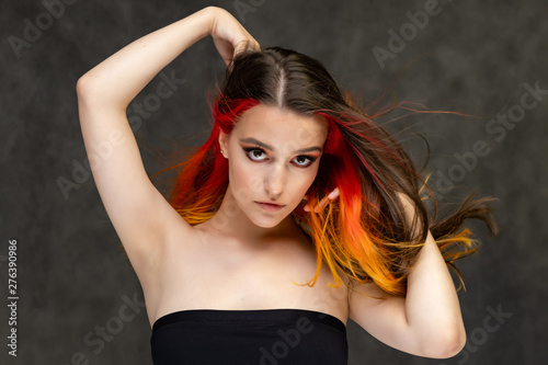 A close-up portrait photo of a fashionable hairstyle red-yellow in studio on a gray background. The pretty brunette model with beautiful make-up has beautiful flowing colorful hair.