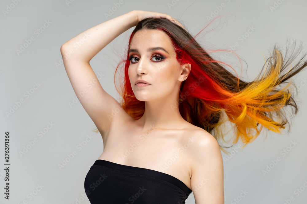 A close-up portrait photo of a fashionable hairstyle red-yellow in studio on a blue background. The pretty brunette model with beautiful make-up has beautiful flowing colorful hair. A close-up portrait photo of a fashionable hairstyle red-yellow in studio on a blue background. The pretty brunette model with beautiful make-up has beautiful flowing colorful hair.