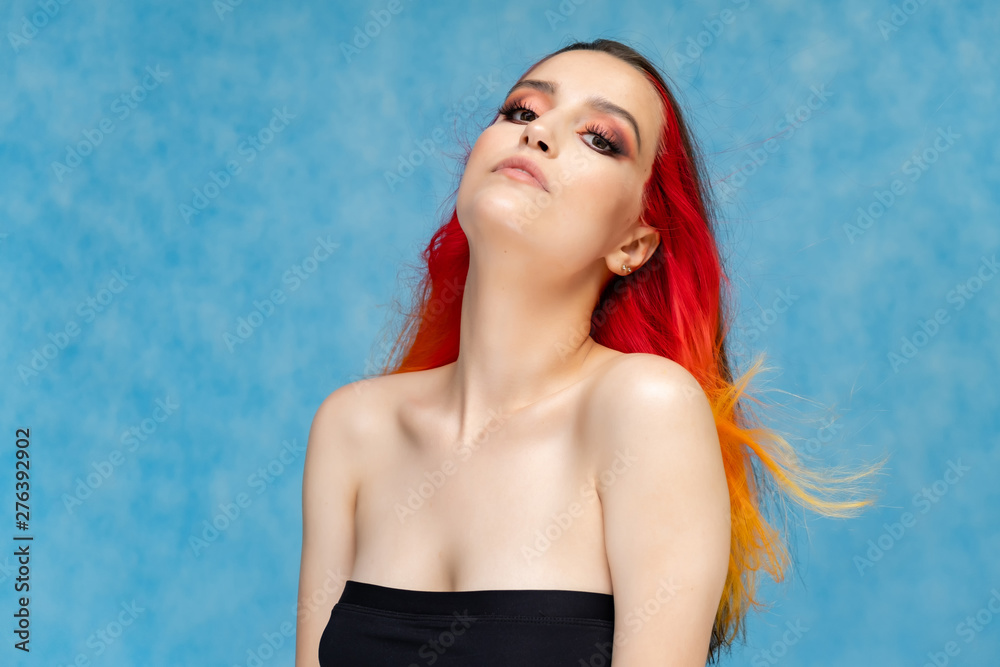 A close-up portrait photo of a fashionable hairstyle red-yellow in studio on a blue background. The pretty brunette model with beautiful make-up has beautiful flowing colorful hair. A close-up portrait photo of a fashionable hairstyle red-yellow in studio on a blue background. The pretty brunette model with beautiful make-up has beautiful flowing colorful hair.