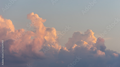 Close up view of beautiful colored cumulus fluffy clouds with pink and purple hues in the blue sky at sunset background