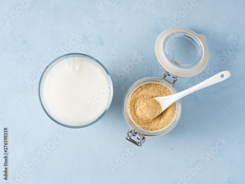 Nutritional yeast and milk. Nutritional inactive yeast in jar and glass of milk on blue tabletop. Copy space. Top view. Nutritional yeast is vegetarian superfood with cheese flavor, for healthy diet