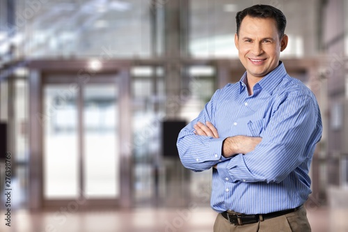 Portrait of handsome middle aged businessman standing with arms crossed on modern city building background