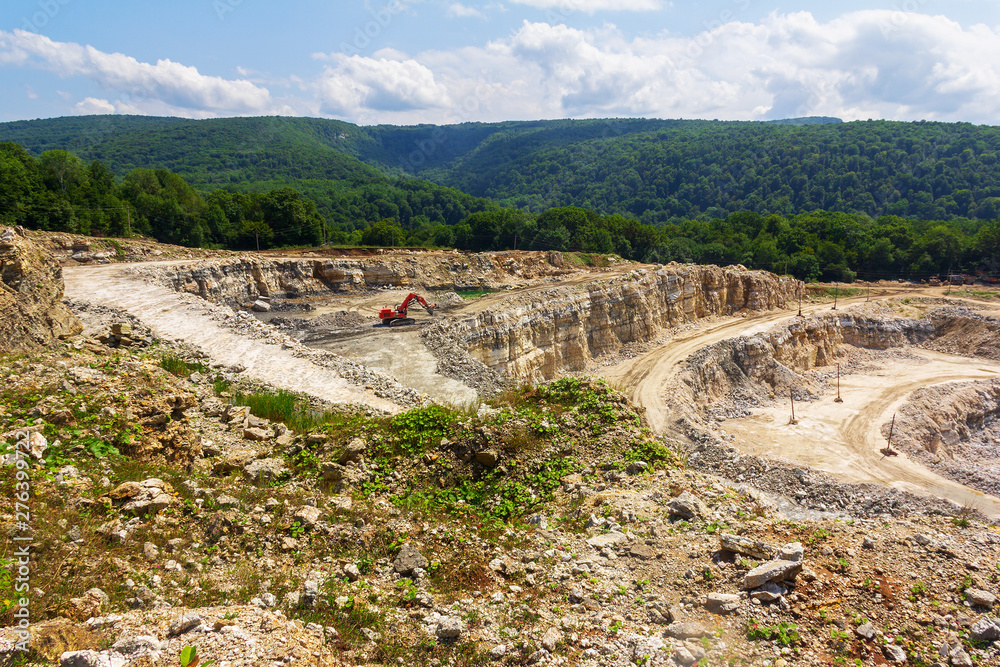 industrial landscape with an excavator in quarry for the extraction of limestone, gypsum and marble on a summer day