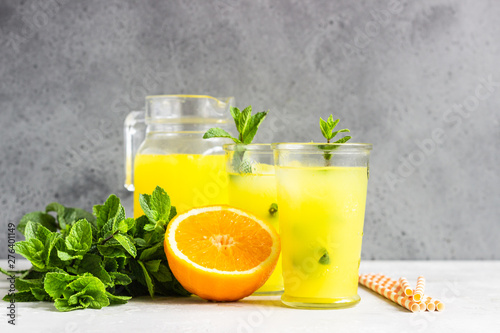 Orange lemonade in glass with fresh orange and mint over light grey stone table. Refreshing summer drink. Cocktail bar background concept. Copy space.