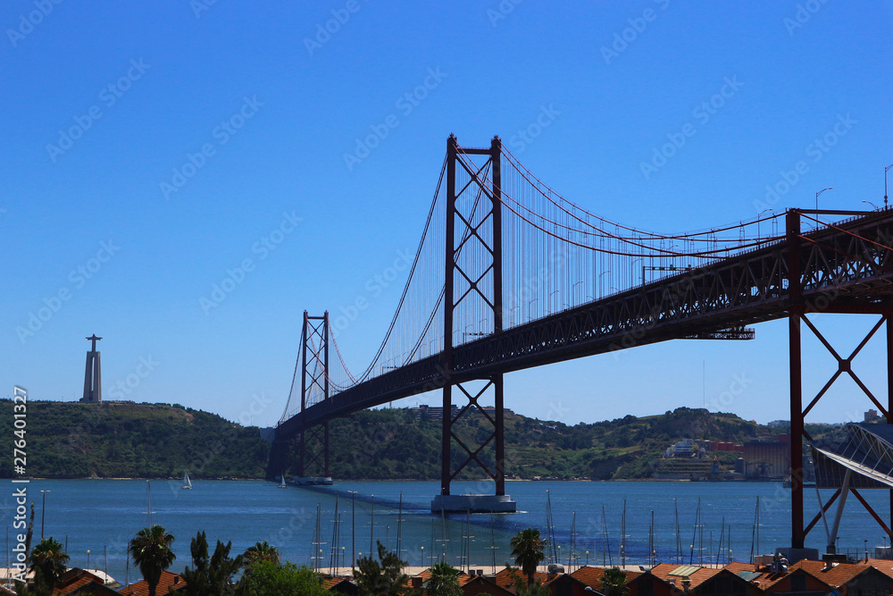 Obraz premium Suspension Bridge over the Tagus or Tejo river with Cristo Rei Sanctuary. Connects the cities of Lisbon and Almada. 25 de Abril Bridge, Lisbon, Portugal.