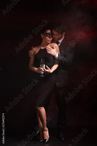 full length view of sensual bdsm couple with glass on champagne embracing on black