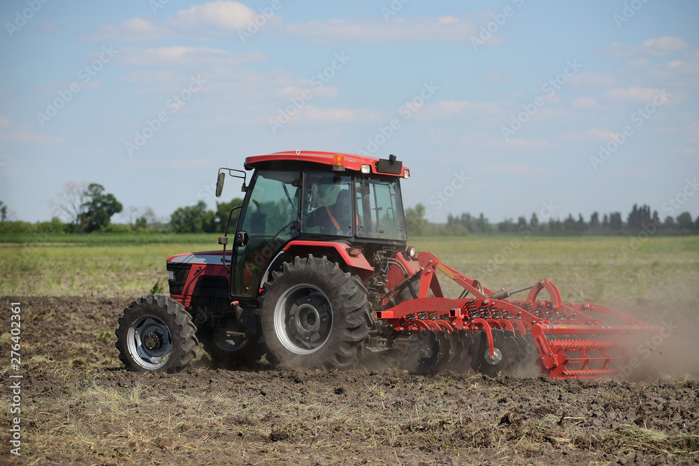 Brand new red tractor on the field working. Tractor cultivating soil and preparing a field for planting Brand new red tractor on the field working. Tractor cultivating soil and preparing a field for planting