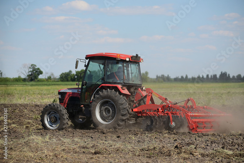 Brand new red tractor on the field working. Tractor cultivating soil and preparing a field for planting