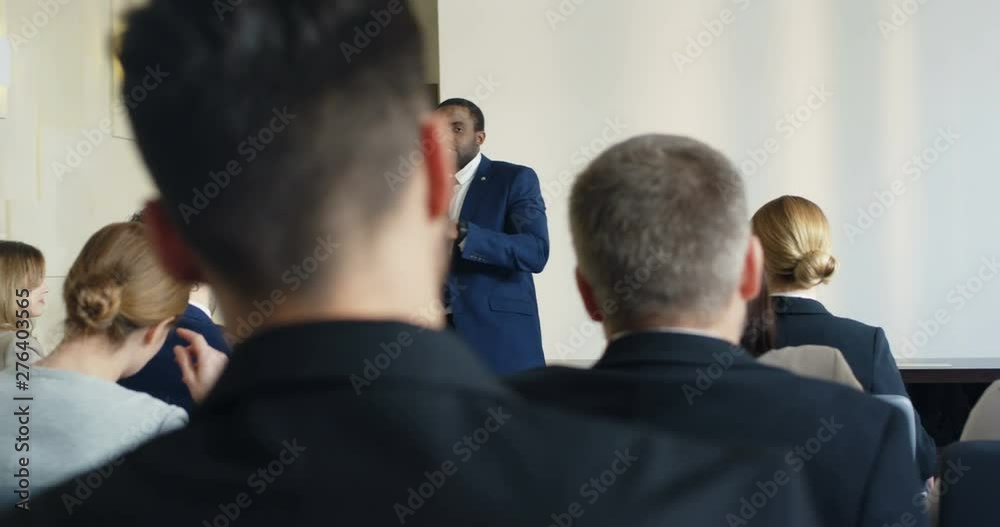 African American good looking young man in glasses talking and coaching in front of mane people during business congress. African American good looking young man in glasses talking and coaching in front of mane people during business congress.