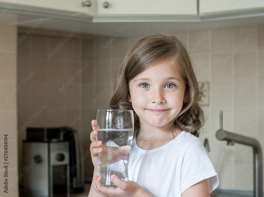 Healthy lifestyle. Portrait of happy smiling young girl with glass. Child drinking fresh water in the kitchen at home, looking at camera. Healthcare. Drinks. Health, beauty, diet concept. Good eating Healthy lifestyle. Portrait of happy smiling young girl with glass. Child drinking fresh water in the kitchen at home, looking at camera. Healthcare. Drinks. Health, beauty, diet concept. Good eating