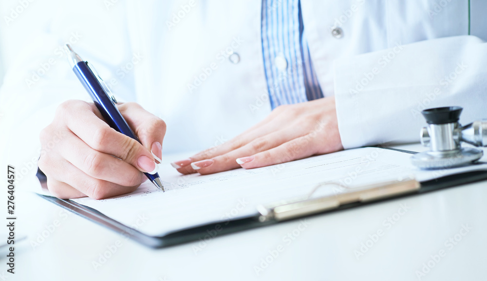 Fototapeta premium Female medicine doctor hand holding silver pen writing something on clipboard close-up.. Ward round, patient visit check, medical calculation and statistics concept.