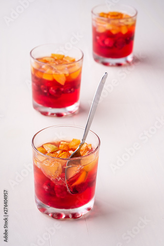 Jelly dessert with fruits apricot raspberry in three drinking glasses with single spoon yellow red summer white background isolated