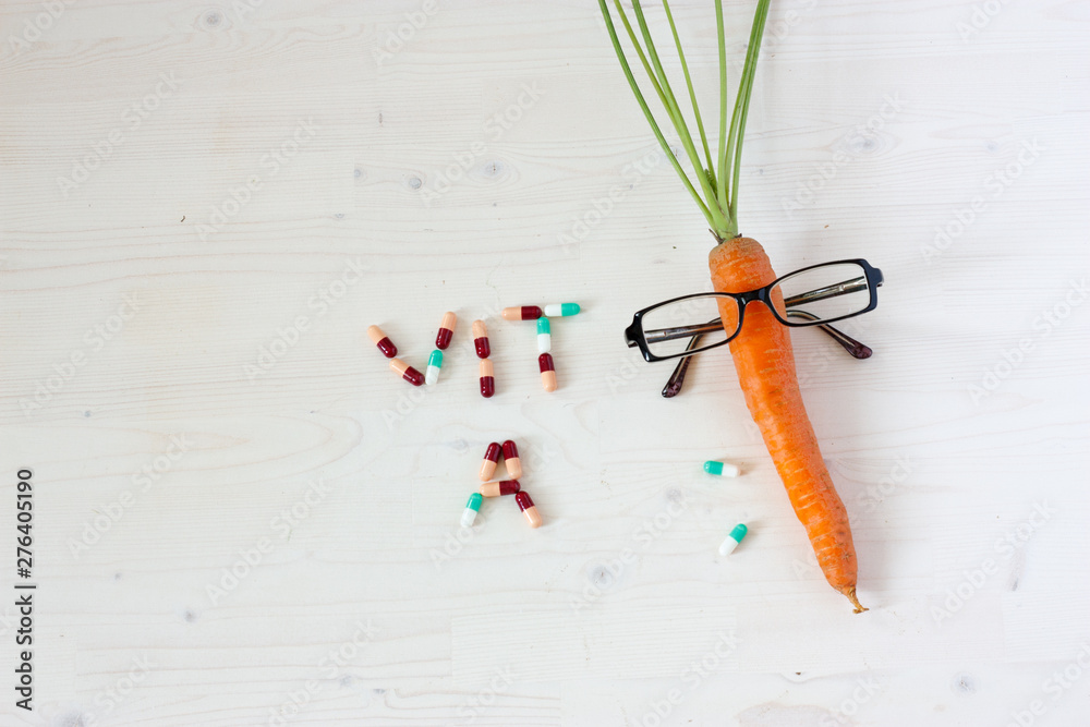 carrot in glasses is on a light wooden background next to the tablets written vitamin A, the left place for the text