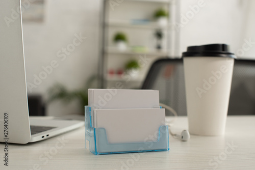 card holder with white blank business cards near paper cup and laptop on office table