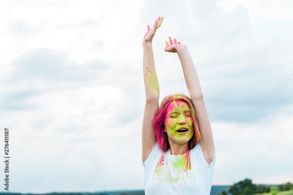 young woman with closed eyes, green and pink holi paint on outstretched hands