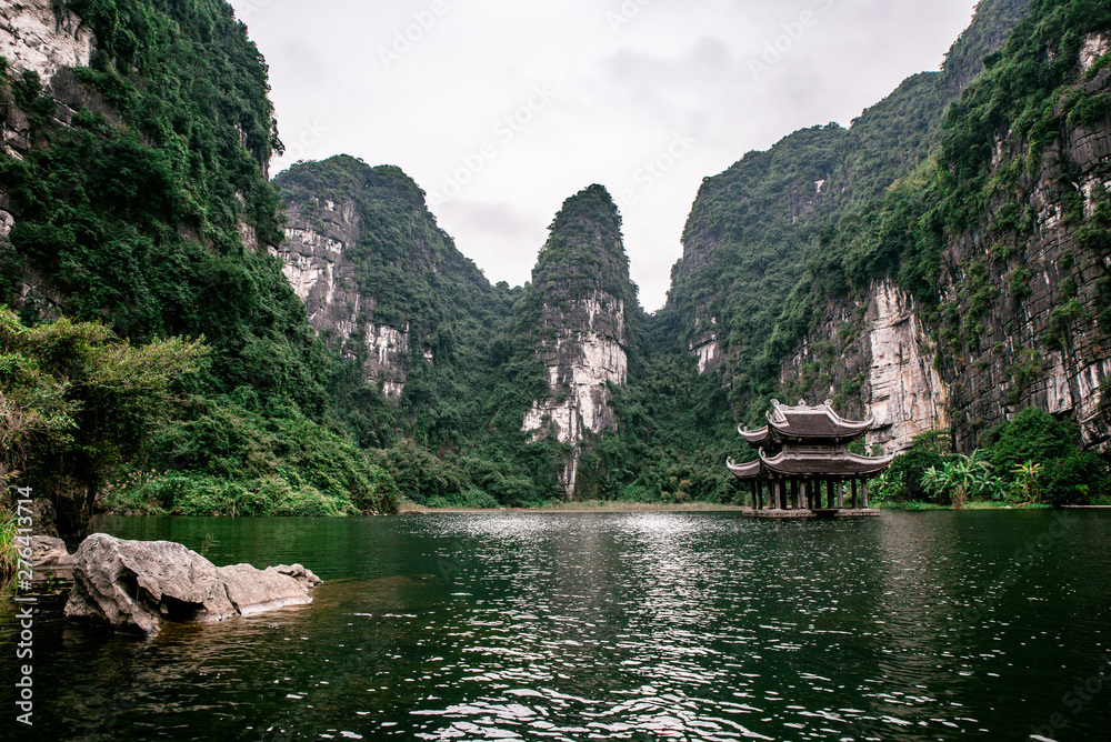 Fototapeta premium Boat cave tour in Trang An Scenic Landscape formed by karst towers and plants along the river (UNESCO World Heritage Site). It's Halong Bay on land of Vietnam. Ninh Binh province, Vietnam.