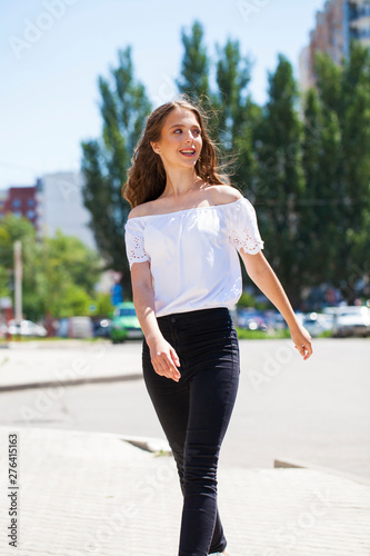 Young beautiful brunette woman in jeans and white blouse walking in summer street © Andrey_Arkusha
