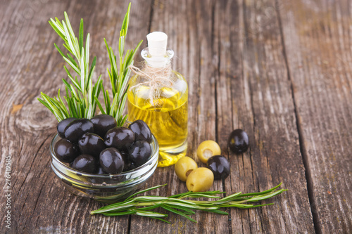 black and green olives a bottle of olive oil and a sprig of rosemary on a wooden background